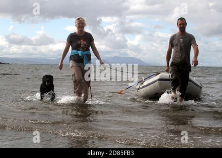 Maidens, Ayrshire, Écosse, Royaume-Uni. Un jeu en famille dans la mer avec un canot en caoutchouc parents adulte tenant avec l'enfant portant un gilet de sauvetage Banque D'Images