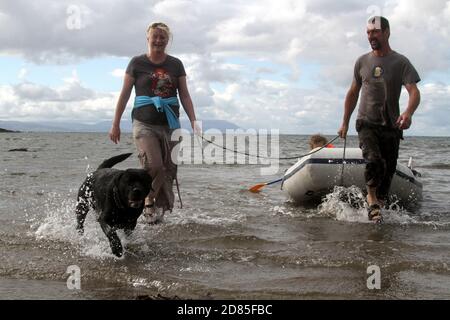 Maidens, Ayrshire, Écosse, Royaume-Uni. Un jeu en famille dans la mer avec un canot en caoutchouc parents adulte tenant avec l'enfant portant un gilet de sauvetage Banque D'Images