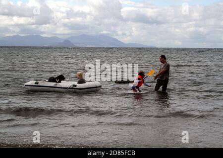 Maidens, Ayrshire, Écosse, Royaume-Uni. Un jeu en famille dans la mer avec un canot en caoutchouc parents adulte tenant avec l'enfant portant un gilet de sauvetage Banque D'Images