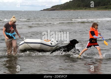 Maidens, Ayrshire, Écosse, Royaume-Uni. Un jeu en famille dans la mer avec un canot en caoutchouc parents adulte tenant avec l'enfant portant un gilet de sauvetage Banque D'Images