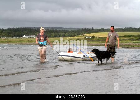 Maidens, Ayrshire, Écosse, Royaume-Uni. Un jeu en famille dans la mer avec un canot en caoutchouc parents adulte tenant avec l'enfant portant un gilet de sauvetage Banque D'Images