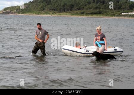 Maidens, Ayrshire, Écosse, Royaume-Uni. Un jeu en famille dans la mer avec un canot en caoutchouc parents adulte tenant avec l'enfant portant un gilet de sauvetage Banque D'Images