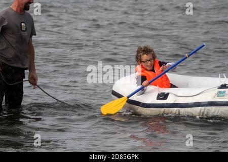 Maidens, Ayrshire, Écosse, Royaume-Uni. Un jeu en famille dans la mer avec un canot en caoutchouc parents adulte tenant avec l'enfant portant un gilet de sauvetage Banque D'Images