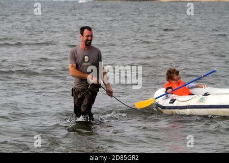 Maidens, Ayrshire, Écosse, Royaume-Uni. Un jeu en famille dans la mer avec un canot en caoutchouc parents adulte tenant avec l'enfant portant un gilet de sauvetage Banque D'Images