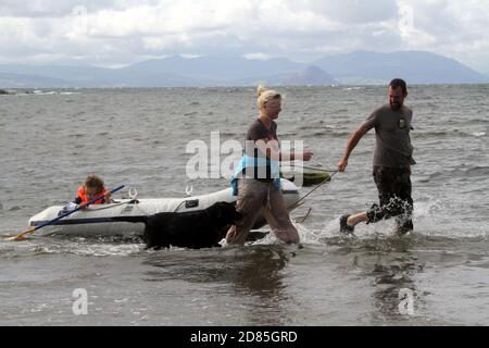 Maidens, Ayrshire, Écosse, Royaume-Uni. Un jeu en famille dans la mer avec un canot en caoutchouc parents adulte tenant avec l'enfant portant un gilet de sauvetage Banque D'Images