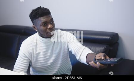 Un homme noir afro-américain excité regardant un match à la télévision, déçu de sauter sur le canapé. Modification du changement de téléviseur Photo de haute qualité Banque D'Images