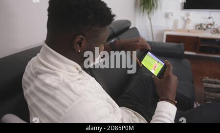 Jeune homme noir excité regardant un match de football sur le smartphone. Photo de haute qualité Banque D'Images
