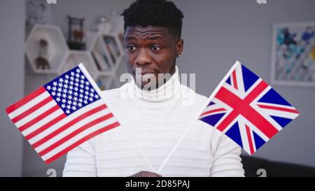 Homme noir confus portant les drapeaux des États-Unis et du Royaume-Uni. Le choix de l'immigration. Photo de haute qualité Banque D'Images