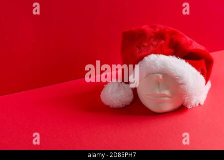 Composition de Noël créative à partir de la tête de sculpture en gypse dans un chapeau rouge du Père Noël sur un fond de corail duotone, espace de copie. Nouveau séjour de vacances concep Banque D'Images