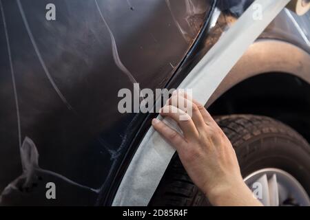 Couvrant la partie en plastique de l'aile du corps d'un voiture noire avec un ruban de protection blanc pour empêcher le pénétration du produit de polissage dans avo Banque D'Images