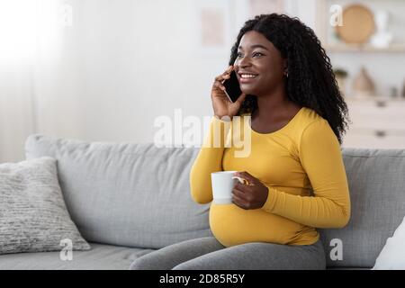 Bonne femme enceinte jeune boire du thé et parler au téléphone Banque D'Images