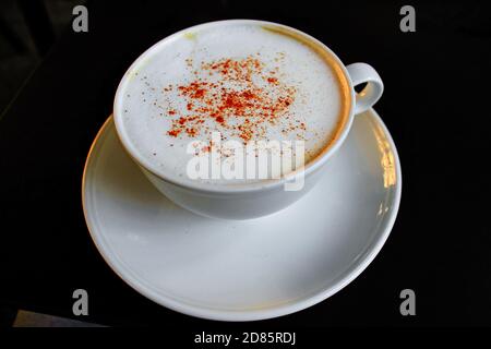 Gros plan de la tasse avec du cappuccino servi avec de la cannelle sur fond noir. Banque D'Images