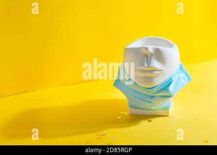 Pot de plâtre en forme de visage humain avec masque médical protecteur sous son menton sur fond jaune avec ombre, espace de copie. Banque D'Images