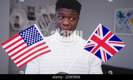 Homme noir confus portant les drapeaux des États-Unis et du Royaume-Uni. Le choix de l'immigration. Photo de haute qualité Banque D'Images