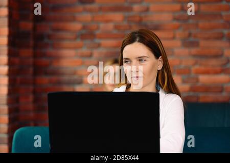 Femme d'affaires dans des vêtements élégants, utiliser un ordinateur portable, et regarde avec ses yeux sur le côté. Nouvel intérieur moderne en brique dans le style loft Banque D'Images