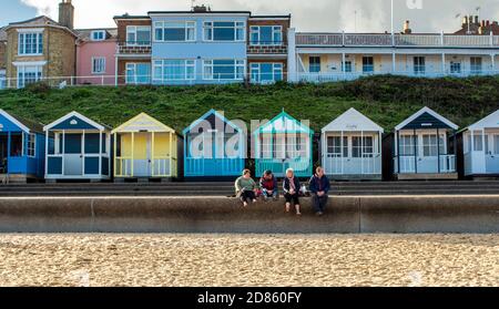 Quatre personnes assises sur la promenade avec des cabanes de plage derrière, Southwold, Suffolk, Royaume-Uni Banque D'Images