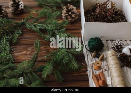 Fabrication d'une couronne de noël rustique sur une table en bois. Couronne de Noël avec baies, branches vertes, cônes de pin et décorations de fête naturelles, ciseaux, t Banque D'Images