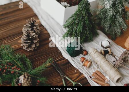 Fabrication d'une couronne de noël rustique sur une table en bois. Couronne de Noël avec baies, branches vertes, cônes de pin et décorations de fête naturelles, ciseaux, t Banque D'Images