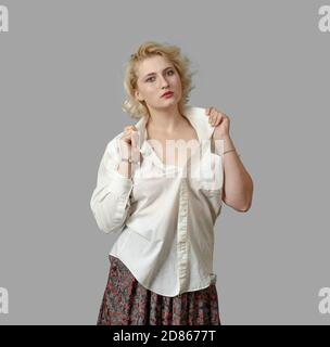 Jeune femme blonde en chemise blanche regarde la caméra, lève son collier sur fond gris. Banque D'Images