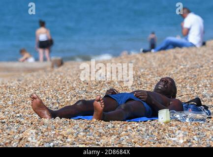 Un homme noir qui s'étend sur une plage lors d'une chaude journée d'été lors de la canicule du 2018 juillet à Brighton, dans l'est du Sussex, en Angleterre, au Royaume-Uni. Banque D'Images