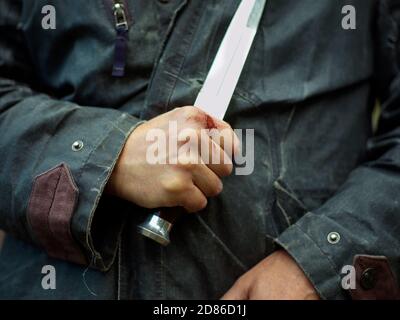 Gros plan d'un homme blessé main avec un couteau géant Banque D'Images