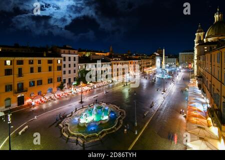 Vue en soirée d'une Piazza Navona illuminée avec le Neptune et la fontaine des quatre fleuves illuminés pendant que les touristes dînent dans les cafés. Banque D'Images