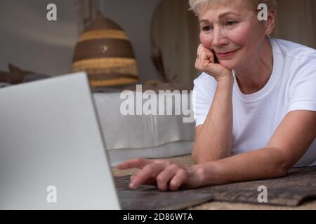 Femme sénior active surfant sur Internet sur un tapis de yoga. Banque D'Images