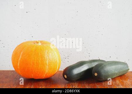 Citrouille orange et deux courgettes vert foncé sur une table en bois sur fond de mur en béton gris. Copier l'espace Banque D'Images