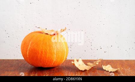 Citrouille orange et feuilles de chêne sec sur une table en bois marron sur fond de mur en béton gris. Espace de copie, composition d'automne Banque D'Images