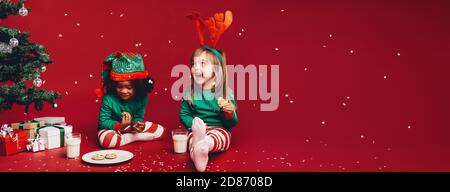 Les petites filles appréciant les flocons de neige tomber assis à côté d'un arbre de Noël. Dans Fantaisie enfants Vêtements de Noël Noël t'asseoir à côté d'une Banque D'Images