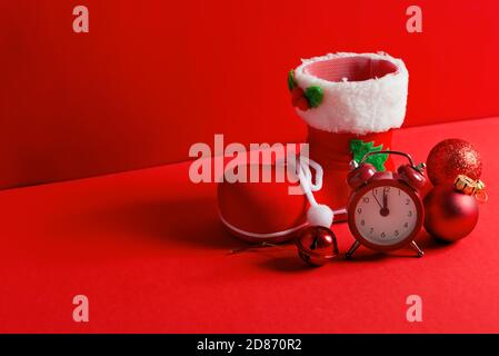 Composition de Noël avec chaussette du Père Noël, décoration festive boules de verre et réveil sur un fond rouge coin , espace de copie. Carte de vœux. Banque D'Images