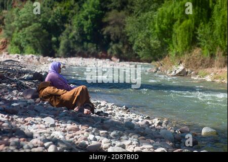 Couple marocain avec djellaba et foulard assis et parler sur la rive d'une rivière à Setti Fatma, dans la vallée de l'Ourika près de Marrakech Banque D'Images