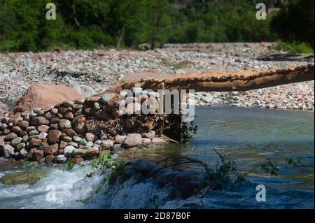 Pont simple de rochers, galets et troncs d'arbres au-dessus d'une rivière à écoulement rapide à Setti Fatma, dans la vallée de l'Ourika près de Marrakech, au Maroc Banque D'Images