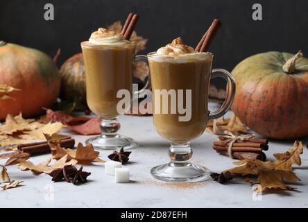 Deux tasses en verre de latte de citrouille aux épices sur fond gris avec citrouilles et feuilles d'automne, gros plan. Banque D'Images