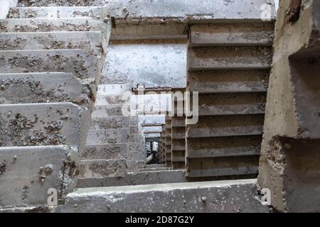Escalier en béton poussiéreux à l'intérieur d'un bâtiment en ruines abandonné. Vue vers le bas tunnel de perspective a traversé la maison de plusieurs étages Banque D'Images
