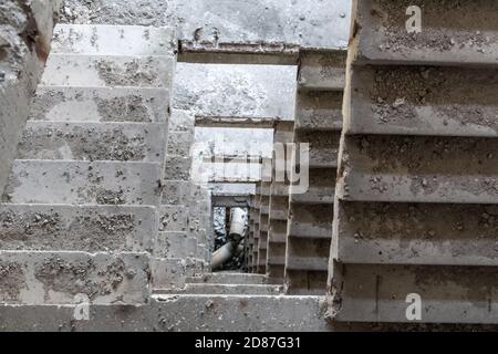 Escalier en béton poussiéreux à l'intérieur d'un bâtiment en ruines abandonné. Vue vers le bas tunnel de perspective a traversé la maison de plusieurs étages Banque D'Images