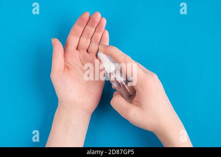 Plan supérieur de POV gros plan au-dessus de la vue photo de la femme mains en appliquant du spray à partir de la petite bouteille sur les mains isolées sur fond bleu de couleur vive Banque D'Images