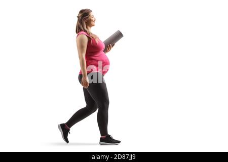 Photo de profil pleine longueur d'une femme enceinte tenue d'un tapis d'exercice et marche isolés sur fond blanc Banque D'Images