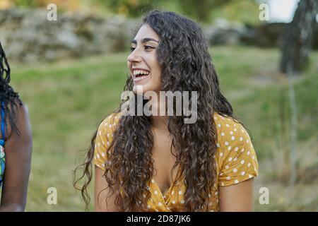 Jeune femme avec des boucles souriant dans un parc portant un blouse jaune Banque D'Images