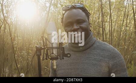Jeune homme noir afro-américain chantant dans le microphone dans les bois. Lumière naturelle. Photo de haute qualité Banque D'Images