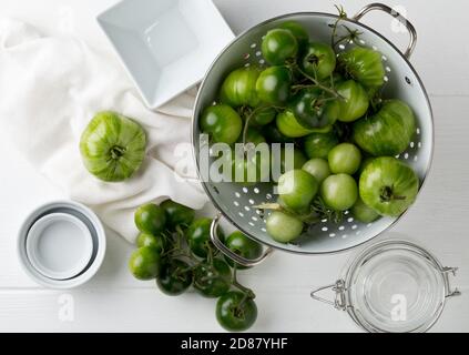 Tomates vertes non mûres en passoire et sur table en bois blanc fond de cuisine, les tomates non mûres peuvent être frites ou utilisées pour la relish, foyer sélectif, f Banque D'Images