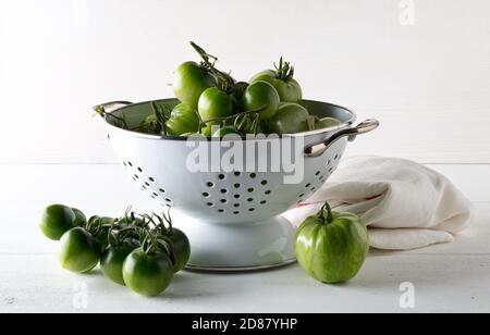 Tomates vertes non mûres en passoire et sur table en bois blanc fond de cuisine, les tomates non mûres peuvent être frites ou utilisées pour la mise au point relish et sélective Banque D'Images