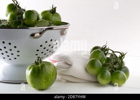 Tomates vertes non mûres en passoire et sur table en bois blanc fond de cuisine, les tomates non mûres peuvent être frites ou utilisées pour la mise au point relish et sélective Banque D'Images