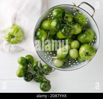 Tomates vertes non mûres en passoire et sur table en bois blanc fond de cuisine, les tomates non mûres peuvent être frites ou utilisées pour la relish, foyer sélectif, f Banque D'Images