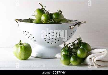 Tomates vertes non mûres en passoire et sur table en bois blanc fond de cuisine, les tomates non mûres peuvent être frites ou utilisées pour la mise au point relish et sélective Banque D'Images