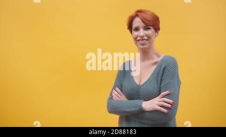 Portrait d'une femme d'âge moyen à tête rouge avec des mains croisées qui se répande, isolée sur fond orange. Photo de haute qualité Banque D'Images