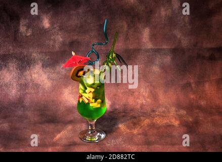 Un verre de boisson verte à base de jus de kiwi et de glace, décoré de pailles et d'un parapluie, se dresse sur un fond sombre. Gros plan. Banque D'Images