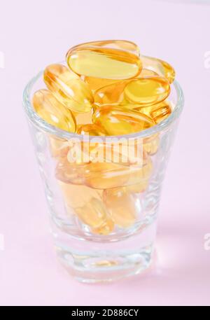 Capsules d'huile de poisson en verre sur fond rose. Banque D'Images