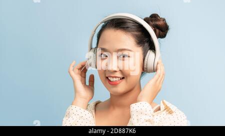 Bonne mignonne jeune femme dans un casque à écouter de la musique arrière-plan bleu Banque D'Images