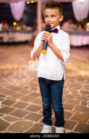 Mignon petit garçon avec le microphone chant pour les invités à la vacances Banque D'Images